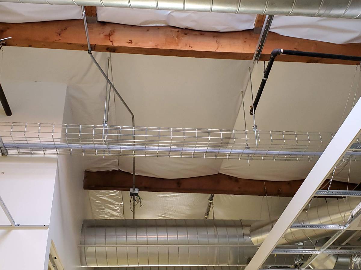 A ceiling with many pipes and wires hanging from it.